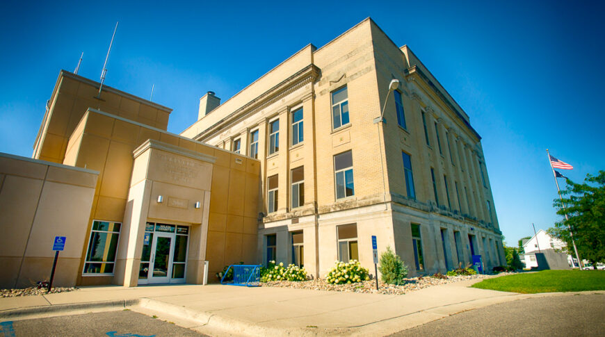 Precast concrete exterior entrance view of Wilkin County Jail building connected to the original government brick building to the right.