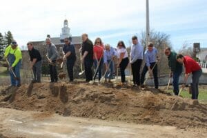 Group of people standing on sand pile shoveling scoops of sand for groundbreaking ceremony for the Fergus Falls Riverfront Phase II project.