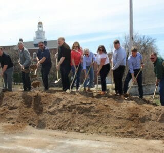 Group of people standing on sand pile shoveling scoops of sand for groundbreaking ceremony for the Fergus Falls Riverfront Phase II project.