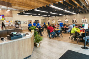 Dining area in Cenex C-Store with small square tables and black chairs with architectural accents overhead and cashier to foreground
