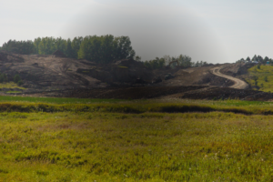 Lake LaMoure spillway reconstruction with grassy fields in foreground and dirt mounds in background with heavy equipment building it back up.