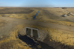 Aerial drone view of a county drainage ditch with a box culvert system and flowing water in the background.