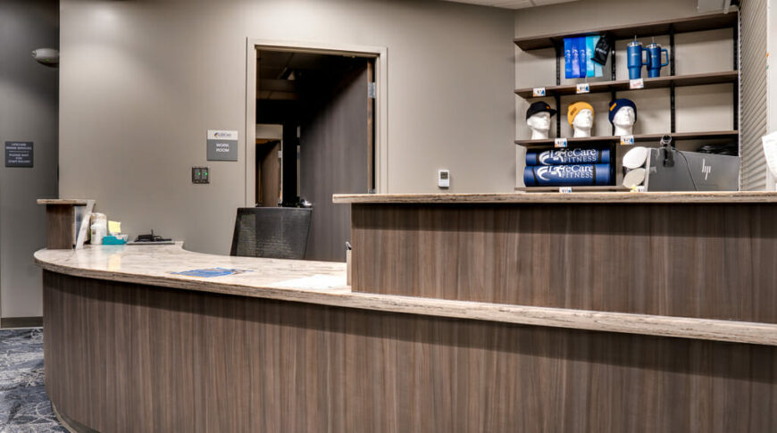 Curved reception desk with two levels with computer stations behind it and a wall of merchandise racks to the back.