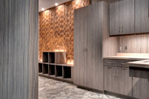 Another room filled with grey/brown cabinetry to the right side, followed down the room with lower cubby cabinetry with wood triangle accent wall.