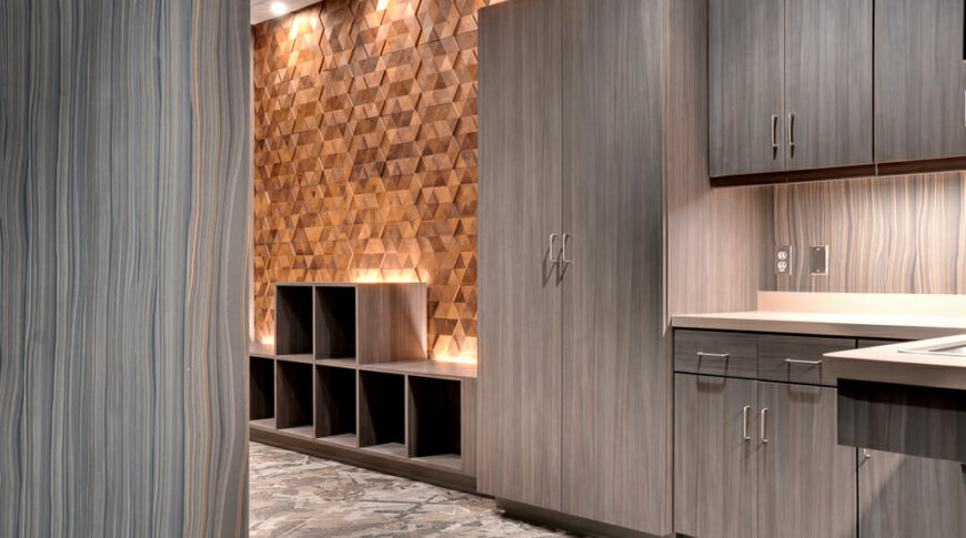 Another room filled with grey/brown cabinetry to the right side, followed down the room with lower cubby cabinetry with wood triangle accent wall.