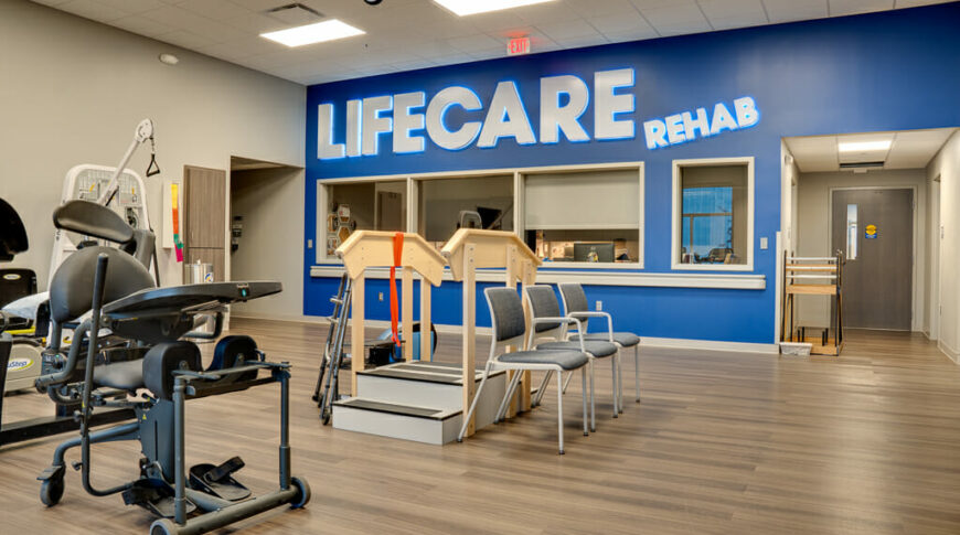 Rehabilitation equipment in big space with blue accent wall to the back with the words "LIFECARE REHAB" in white backlit sign.