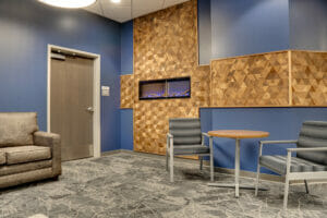 Waiting area with couch to back left wall, small table with two chairs to back right, flanked by blue accent wall with fireplace and custom cross-shaped wooden triangle accent.