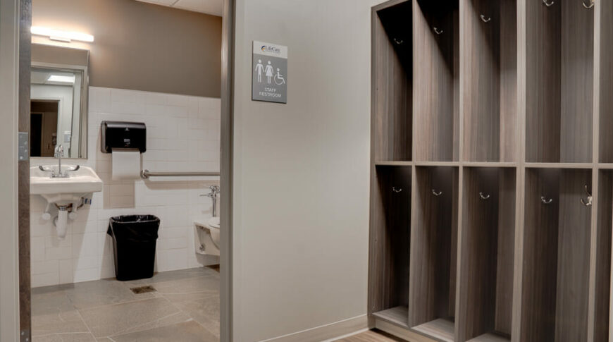 Open double-stacked locker spaces next to bathroom opening where we can see a sink and part of a toilet.