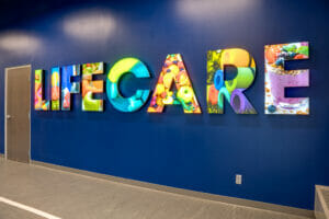 Blue feature wall of fitness center with the words "LIFECARE" lit up in colorful health imagery.