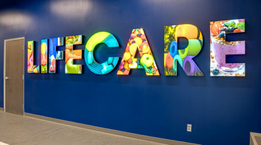 Blue feature wall of fitness center with the words "LIFECARE" lit up in colorful health imagery.