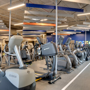 Inside of newly renovated gym with aerobic equipment in middle with vibrant blue wall to the back with lit "LIFECARE" marquee on it.