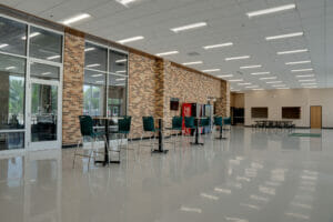 School commons area with light flooring with tall tables and chairs, vending machines in the background and brown brick wall behind.