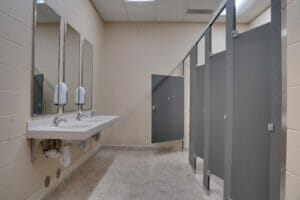 Newly renovated bathroom with gray stalls, light-colored vanity, beige walls and light tiled floors.
