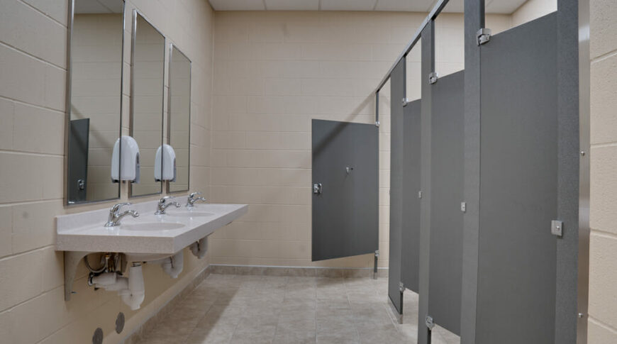 Newly renovated bathroom with gray stalls, light-colored vanity, beige walls and light tiled floors.