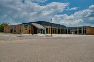 Exterior view of Thompson School addition with brown brick and gray metal exterior and green "TT" school marquee and parking lot to the foreground.