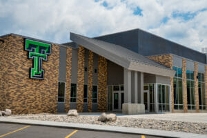 Exterior view of Thompson School addition with brown brick and gray metal exterior and green "TT" school marquee.