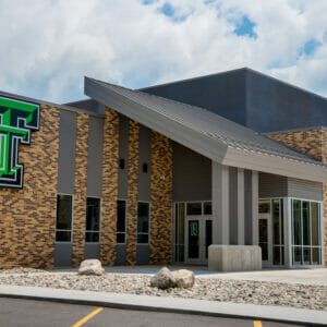 Exterior view of Thompson School addition with brown brick and gray metal exterior and green "TT" school marquee.