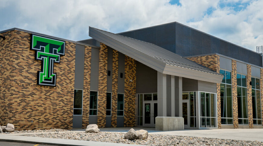 Exterior view of Thompson School addition with brown brick and gray metal exterior and green "TT" school marquee.