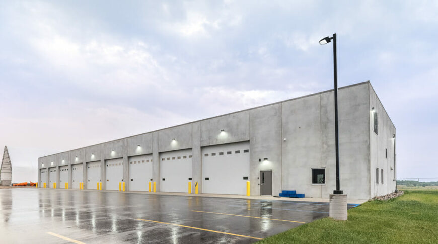Exterior of concrete truck bay building with 9 truck bays and parking lot in front.