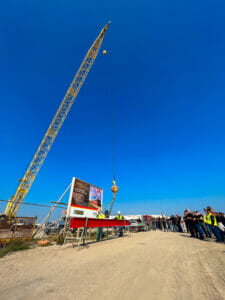 Red structural beam being connected to crane to lift into final resting place.