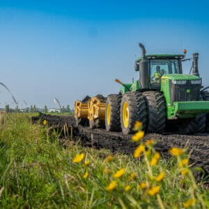 View from in wildflower field looking at oncoming green tractor with scraper attachment that's developing the land for the Rivers Edge Second Addition project.