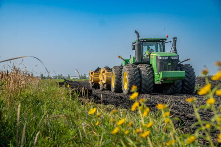 View from in wildflower field looking at oncoming green tractor with scraper attachment that's developing the land for the Rivers Edge Second Addition project.