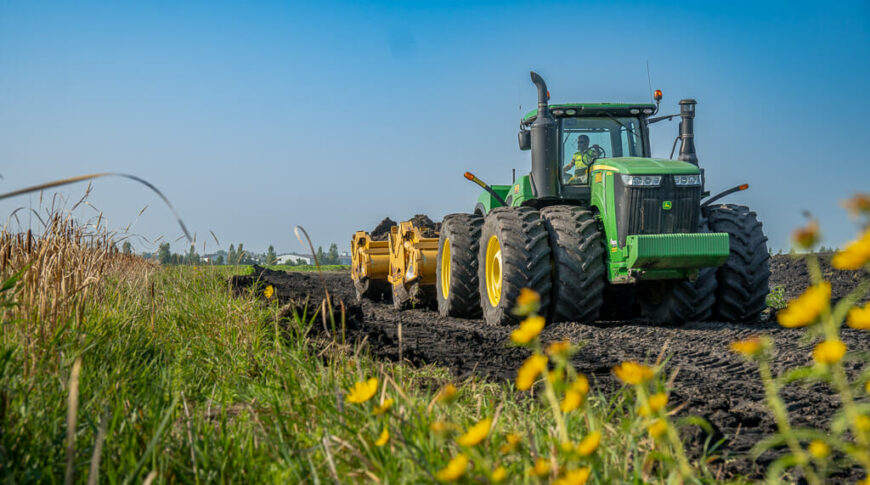 City of Horace-Civil Construction-Low Res-12 View from in wildflower field looking at oncoming green tractor with scraper attachment that's developing the land for the Rivers Edge Second Addition project.