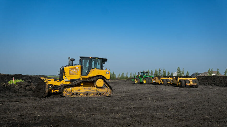 City of Horace-Civil Construction-Low Res-9 Yellow bulldozer in foreground with green tractor with scraper attachments in background of a black dirt field with blue sky above.