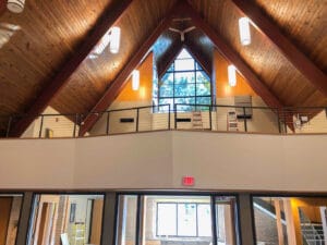 View of church looking from ground floor up to second floor balcony and a-framed wooden shiplap ceiling above.