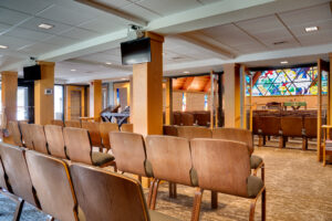 Overflow seating area of lutheran church chapel with double glass framed doors leading into the main sanctuary space.