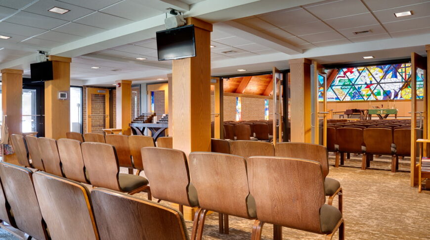 Overflow seating area of lutheran church chapel with double glass framed doors leading into the main sanctuary space.