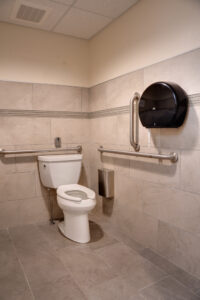 Interior of newly renovated ADA accessible bathroom with toilet, rai bars, receptacle and toilet paper dispensor.