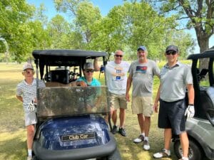 Three men and two young boys standing around a golf cart smiling for a picture.