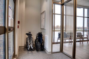 Double door entryway to the Sanford Horace Clinic with automatic sliding doors and floor to ceiling windows viewing reception area. Two folded wheelchairs in the corner for convenience.