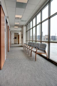 Clinic hallway looking down with patient exam rooms on the left side with sliding barn doors and a wall of windows to the right with waiting chairs lining it.