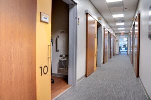 Grey carpeted corridor with numbered exam rooms with sliding barn doors on either side.
