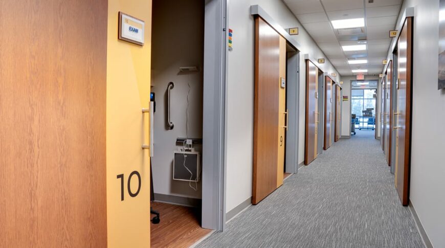 Grey carpeted corridor with numbered exam rooms with sliding barn doors on either side.