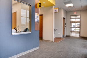 Intersection of clinic hallways. One on the far right leading to the entryway and one in the middle leading to blood draw and exam rooms. Window to the left wall and water fountain across the hall.
