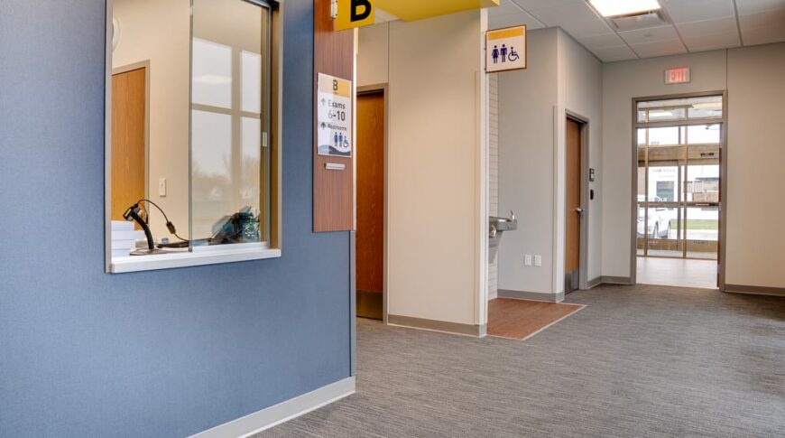 Intersection of clinic hallways. One on the far right leading to the entryway and one in the middle leading to blood draw and exam rooms. Window to the left wall and water fountain across the hall.