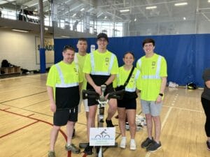 Five people in safety green shirts and shorts standing around an exercise bike for a charity race event.