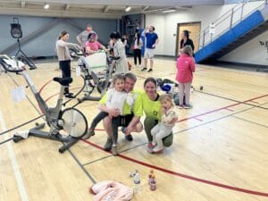 Family with mom and dad kneeling down holding a toddler on each parent with an exercise gym in the background.