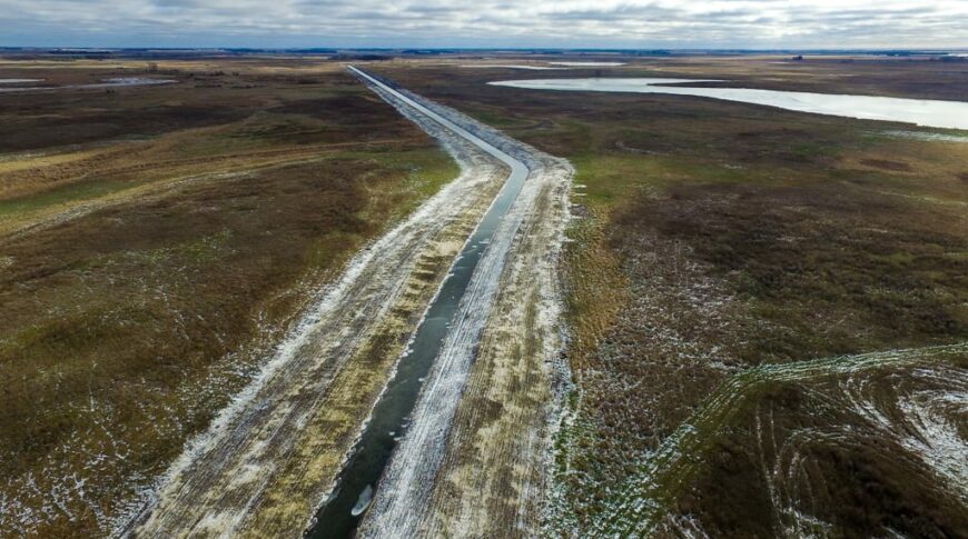 View from the air of a newly excavated and regraded drainage ditch running through pasture and farmland.