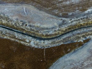 Overhead view looking down at a bend in a county drainage ditch filled with blue water running across pasture land.