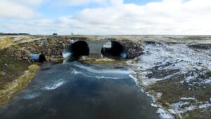 Ground-level view of double culvert underneath road with partially frozen water running underneath.