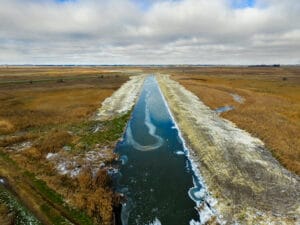 Aerial view of a straight drainage ditch that has recently been excavated with dark blue water running throughout during the fall season.