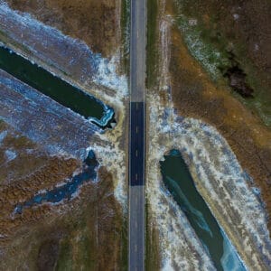 View from the air looking straight down overhead a newly paved road section with drainage ditch with water running on either side