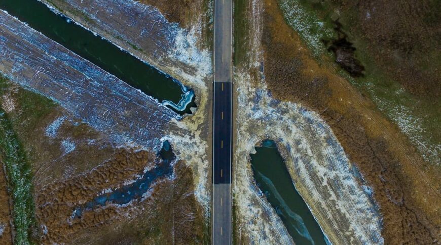 View from the air looking straight down overhead a newly paved road section with drainage ditch with water running on either side