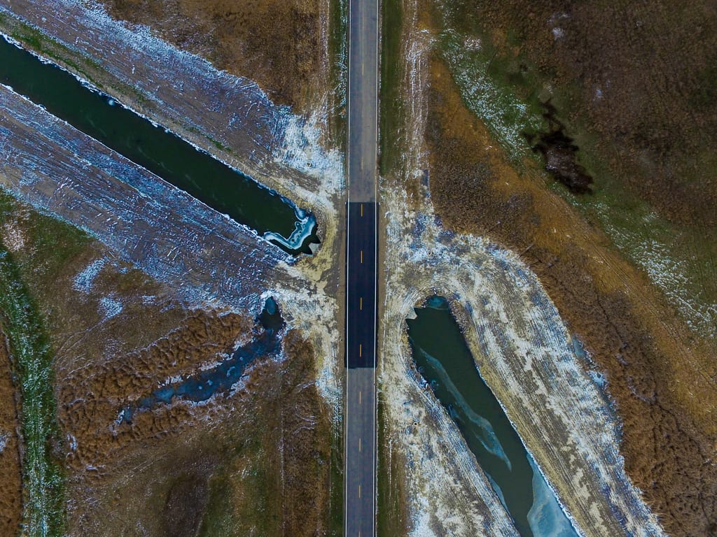 View from the air looking straight down overhead a newly paved road section with drainage ditch with water running on either side