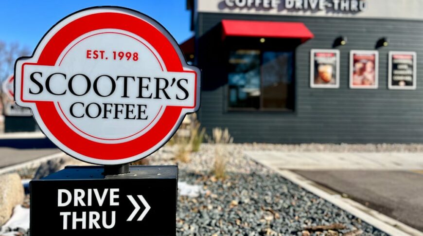 Up-close view of a small Scooter's Coffee Drive-Thru sign with the coffee building blurred behind it.