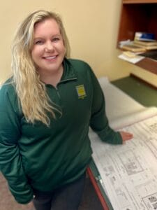 Young woman with long blonde curly hair standing with construction plans on the table beneath her.